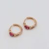 Gold-plated hoop earrings with intricate chain details and bold pink gemstone centers, displayed on a neutral background.
