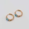 Gold-plated hoop earrings with intricate chain details and bold aqua gemstone centers, displayed on a neutral background.
