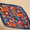 A vibrant kaleidoscope-patterned scarf with bold circular designs in red, blue, and orange, featuring a pleated texture, displayed on a wooden surface.