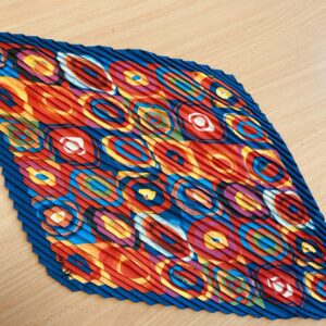 A vibrant kaleidoscope-patterned scarf with bold circular designs in red, blue, and orange, featuring a pleated texture, displayed on a wooden surface.